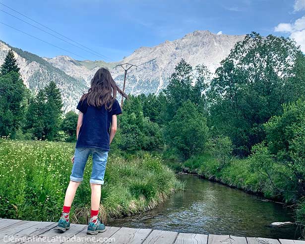 Petit Lutin observe le ruisseau, dans un cadre montagneux.
