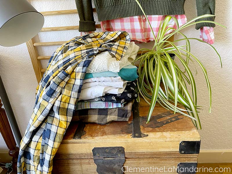 Mise en scène d'une pile de vêtements sur un coffre en bois pour illustrer le sujet des gardes robes minimaliste